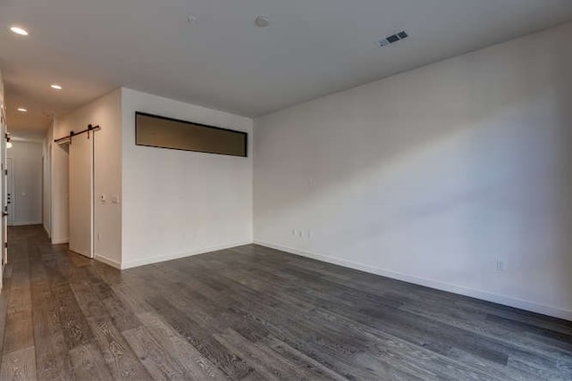 empty room with dark wood-type flooring and a barn door