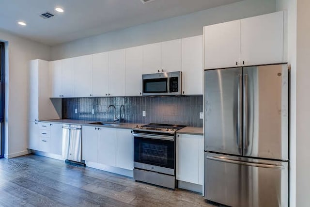 kitchen with sink, appliances with stainless steel finishes, tasteful backsplash, white cabinets, and dark hardwood / wood-style flooring