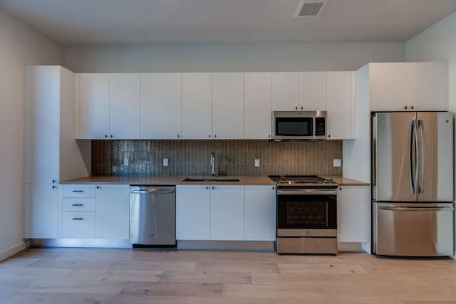 kitchen with stainless steel appliances, white cabinetry, sink, and decorative backsplash