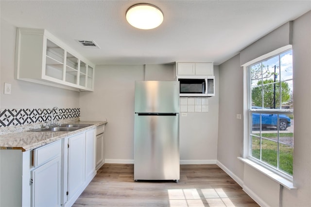 kitchen featuring light hardwood / wood-style flooring, stainless steel refrigerator, white cabinetry, and light stone counters