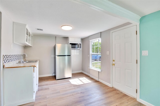 kitchen featuring appliances with stainless steel finishes, white cabinetry, sink, and light hardwood / wood-style flooring