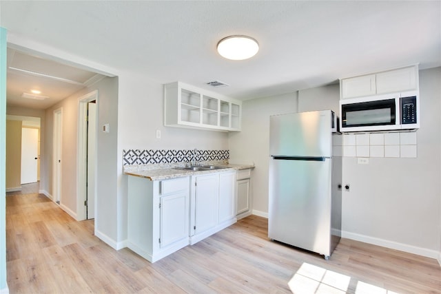 kitchen with sink, light wood-type flooring, white cabinets, light stone counters, and fridge