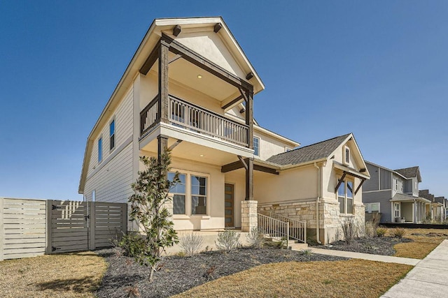 view of front facade featuring a balcony, stone siding, and stucco siding