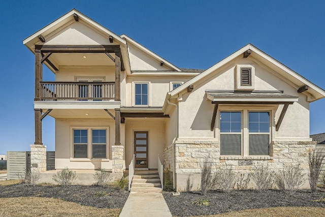 view of front facade featuring a balcony, stucco siding, and stone siding