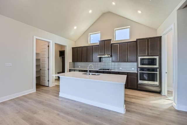 kitchen featuring appliances with stainless steel finishes, a sink, dark brown cabinets, light countertops, and backsplash