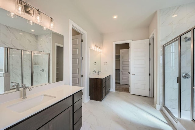 bathroom with marble look tiles, a spacious closet, a marble finish shower, and two vanities
