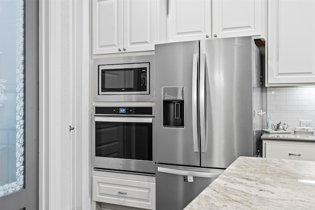 kitchen featuring white cabinets, appliances with stainless steel finishes, light stone countertops, and backsplash