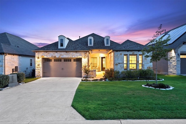 french provincial home featuring an attached garage, concrete driveway, a front lawn, and stone siding