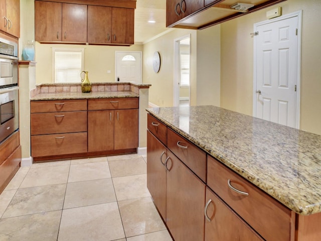 kitchen with a healthy amount of sunlight, ornamental molding, light tile floors, and light stone counters