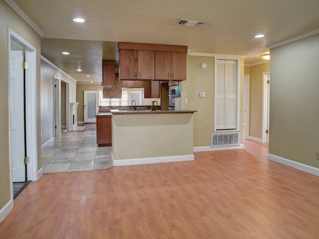 kitchen with dark stone countertops, kitchen peninsula, light wood-type flooring, and crown molding