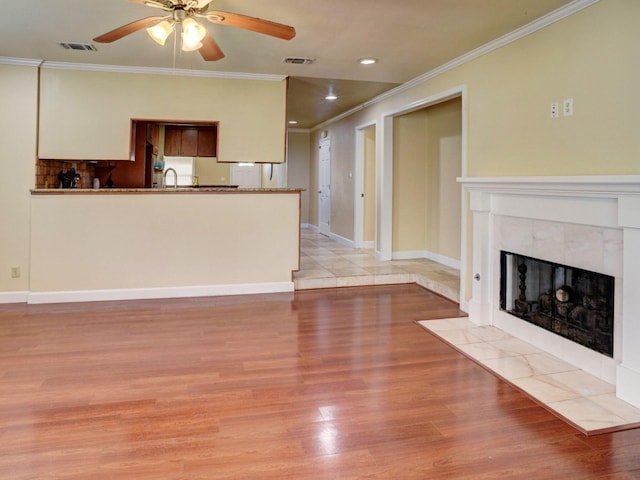 unfurnished living room featuring crown molding, light hardwood / wood-style flooring, ceiling fan, and a fireplace