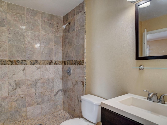 bathroom featuring tiled shower, vanity with extensive cabinet space, and toilet