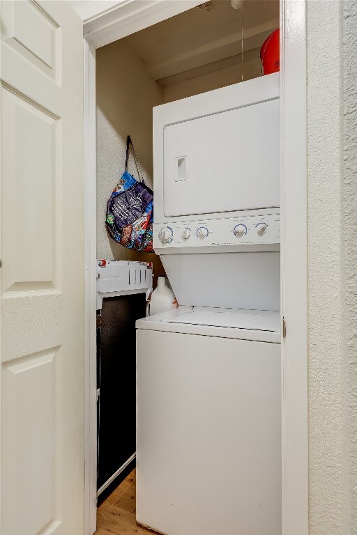 laundry area with stacked washing maching and dryer and light hardwood / wood-style flooring