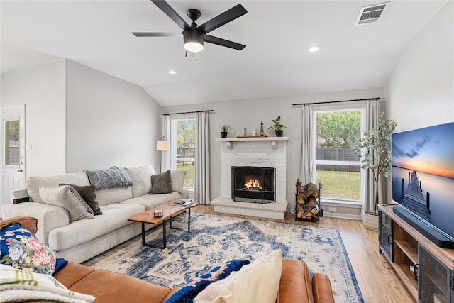 living room featuring light hardwood / wood-style floors, a fireplace, ceiling fan, and lofted ceiling