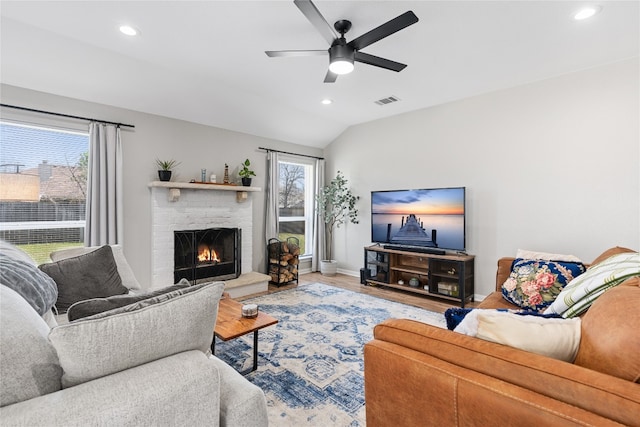 living room with ceiling fan, a brick fireplace, light hardwood / wood-style flooring, and vaulted ceiling