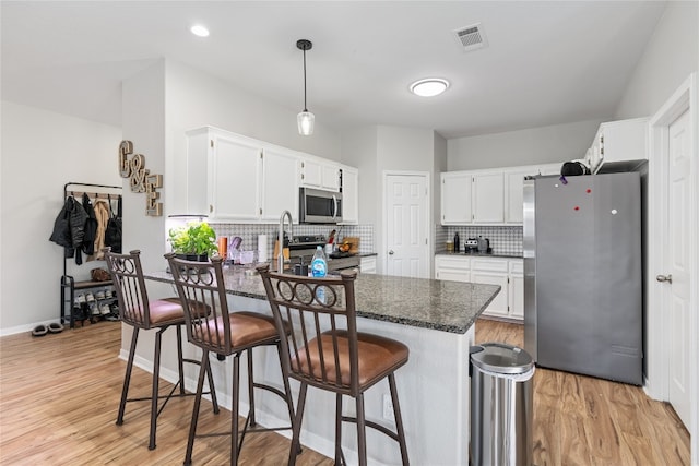 kitchen with stainless steel appliances, dark stone counters, tasteful backsplash, light hardwood / wood-style flooring, and white cabinets