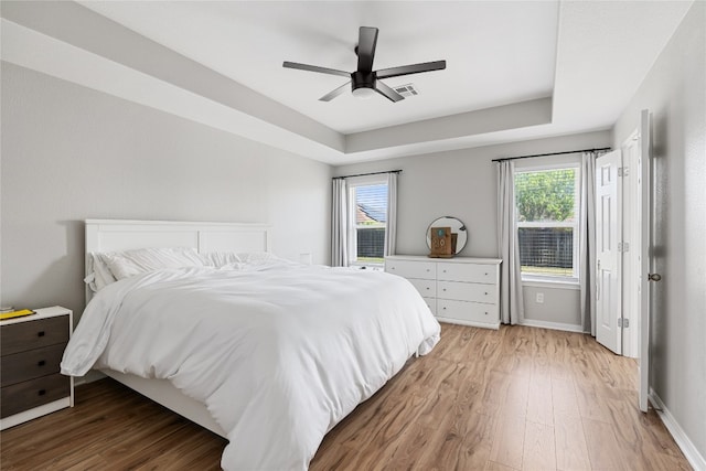 bedroom featuring ceiling fan, light wood-type flooring, and a raised ceiling