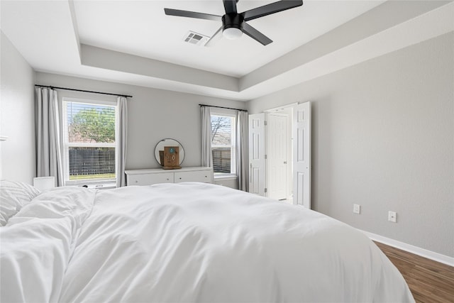 bedroom featuring multiple windows, a raised ceiling, ceiling fan, and wood-type flooring