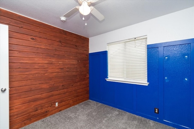 unfurnished room with wooden walls, dark carpet, and ceiling fan