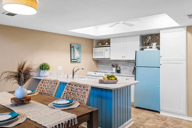 kitchen with kitchen peninsula, decorative backsplash, white cabinets, sink, and white appliances