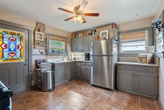 kitchen with backsplash, gray cabinetry, ceiling fan, and stainless steel fridge