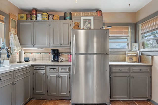 kitchen featuring backsplash, gray cabinetry, sink, and stainless steel refrigerator