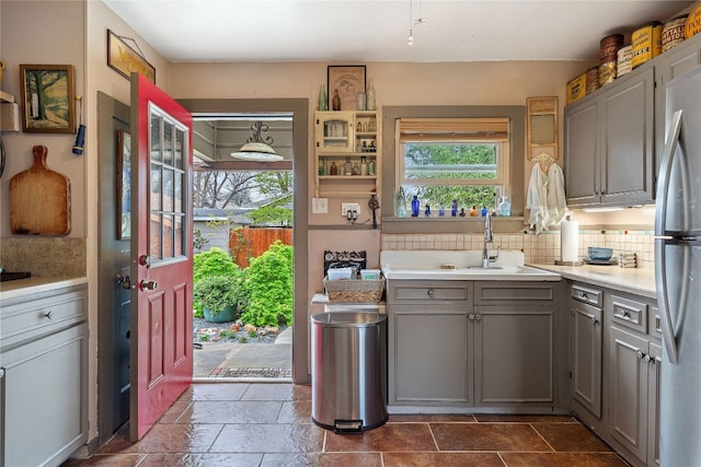 kitchen featuring decorative light fixtures, gray cabinets, tasteful backsplash, dark tile flooring, and stainless steel refrigerator