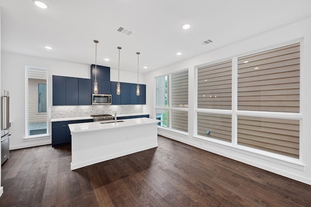 kitchen featuring blue cabinets, sink, appliances with stainless steel finishes, pendant lighting, and a kitchen island with sink