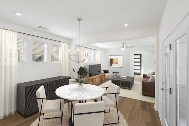 dining space with ceiling fan with notable chandelier and hardwood / wood-style flooring