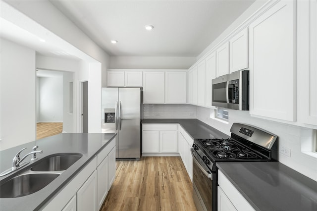 kitchen with appliances with stainless steel finishes, light hardwood / wood-style flooring, white cabinets, and sink