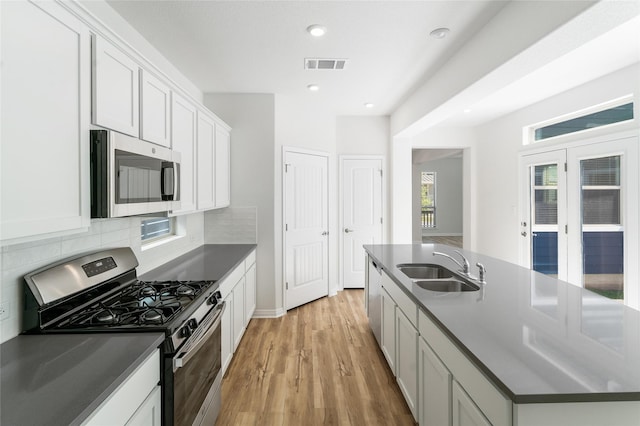 kitchen featuring appliances with stainless steel finishes, decorative backsplash, light wood-type flooring, white cabinets, and sink