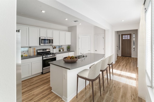 kitchen with white cabinets, a kitchen bar, appliances with stainless steel finishes, and light hardwood / wood-style floors