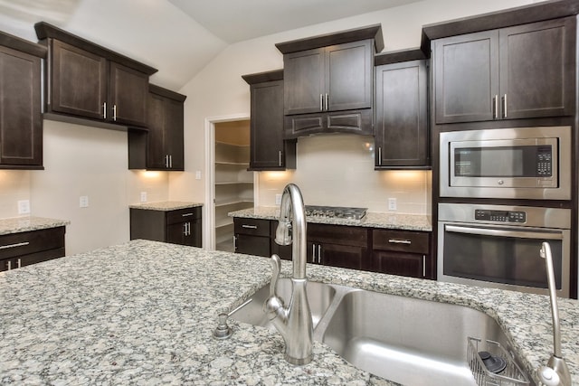 kitchen with backsplash, dark brown cabinetry, stainless steel appliances, and light stone counters