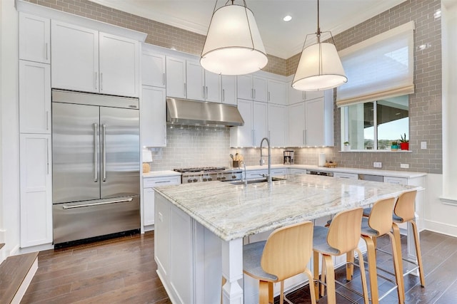 kitchen featuring sink, hanging light fixtures, stainless steel appliances, white cabinets, and a center island with sink