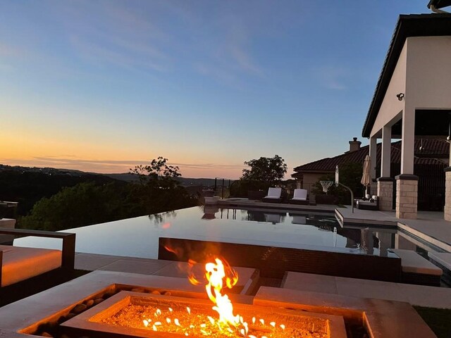 pool at dusk with a fire pit and a patio