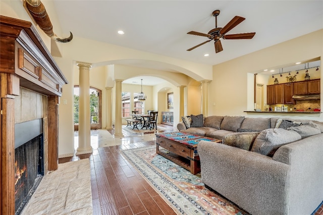 living room featuring decorative columns, light wood-type flooring, and ceiling fan with notable chandelier