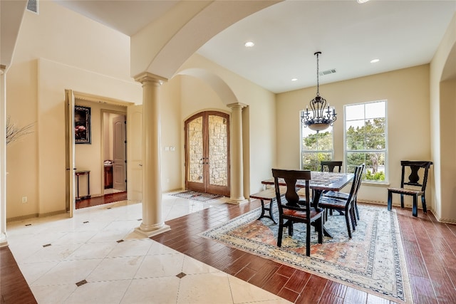 dining space featuring light wood-type flooring, french doors, ornate columns, and a chandelier