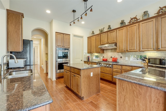 kitchen with backsplash, appliances with stainless steel finishes, sink, a center island, and dark stone counters