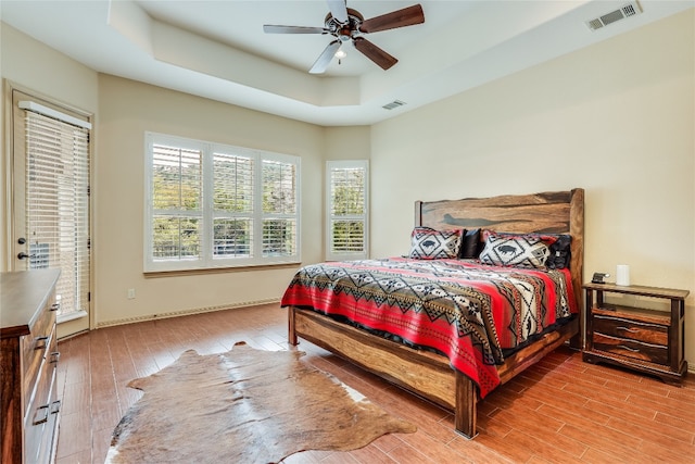 bedroom with ceiling fan, light hardwood / wood-style flooring, and a raised ceiling