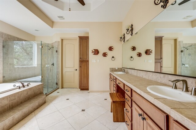 bathroom with double sink, oversized vanity, separate shower and tub, ceiling fan, and a raised ceiling