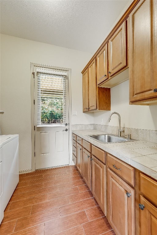 kitchen featuring a textured ceiling, sink, washing machine and dryer, and light wood-type flooring