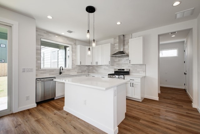 kitchen featuring white cabinets, appliances with stainless steel finishes, a kitchen island, and wall chimney range hood