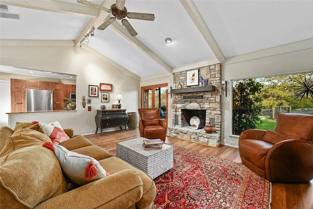 living room with plenty of natural light, a stone fireplace, light wood-type flooring, and beam ceiling