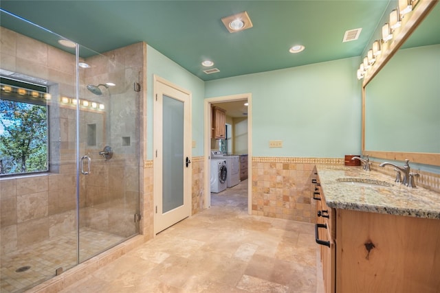 bathroom with vanity, tile walls, a shower with shower door, and washing machine and clothes dryer