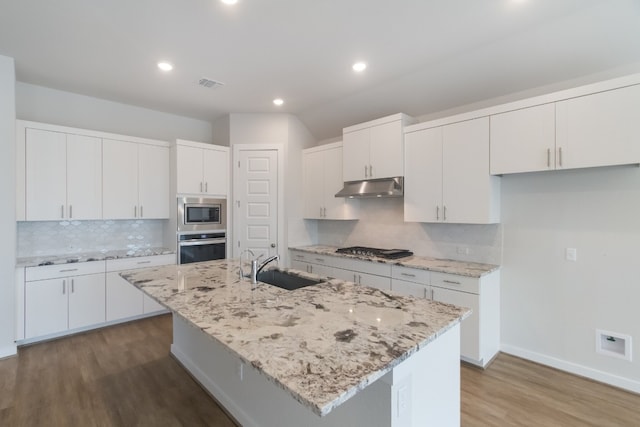 kitchen with white cabinets, light hardwood / wood-style flooring, tasteful backsplash, and an island with sink