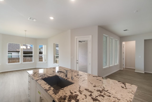 kitchen with a notable chandelier, sink, dark wood-type flooring, and light stone counters