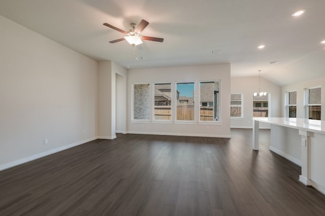 unfurnished living room featuring ceiling fan with notable chandelier, vaulted ceiling, and dark wood-type flooring