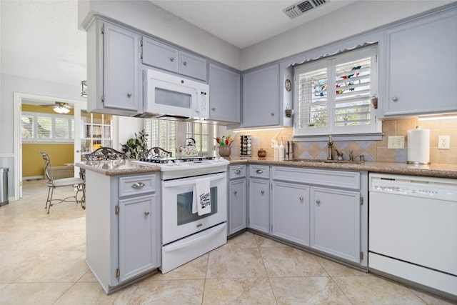 kitchen with a sink, white appliances, plenty of natural light, gray cabinets, and visible vents