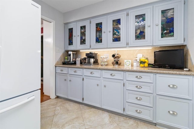 kitchen with freestanding refrigerator, light tile patterned floors, glass insert cabinets, and tasteful backsplash