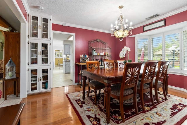 dining area with crown molding, a notable chandelier, a textured ceiling, and light hardwood / wood-style flooring